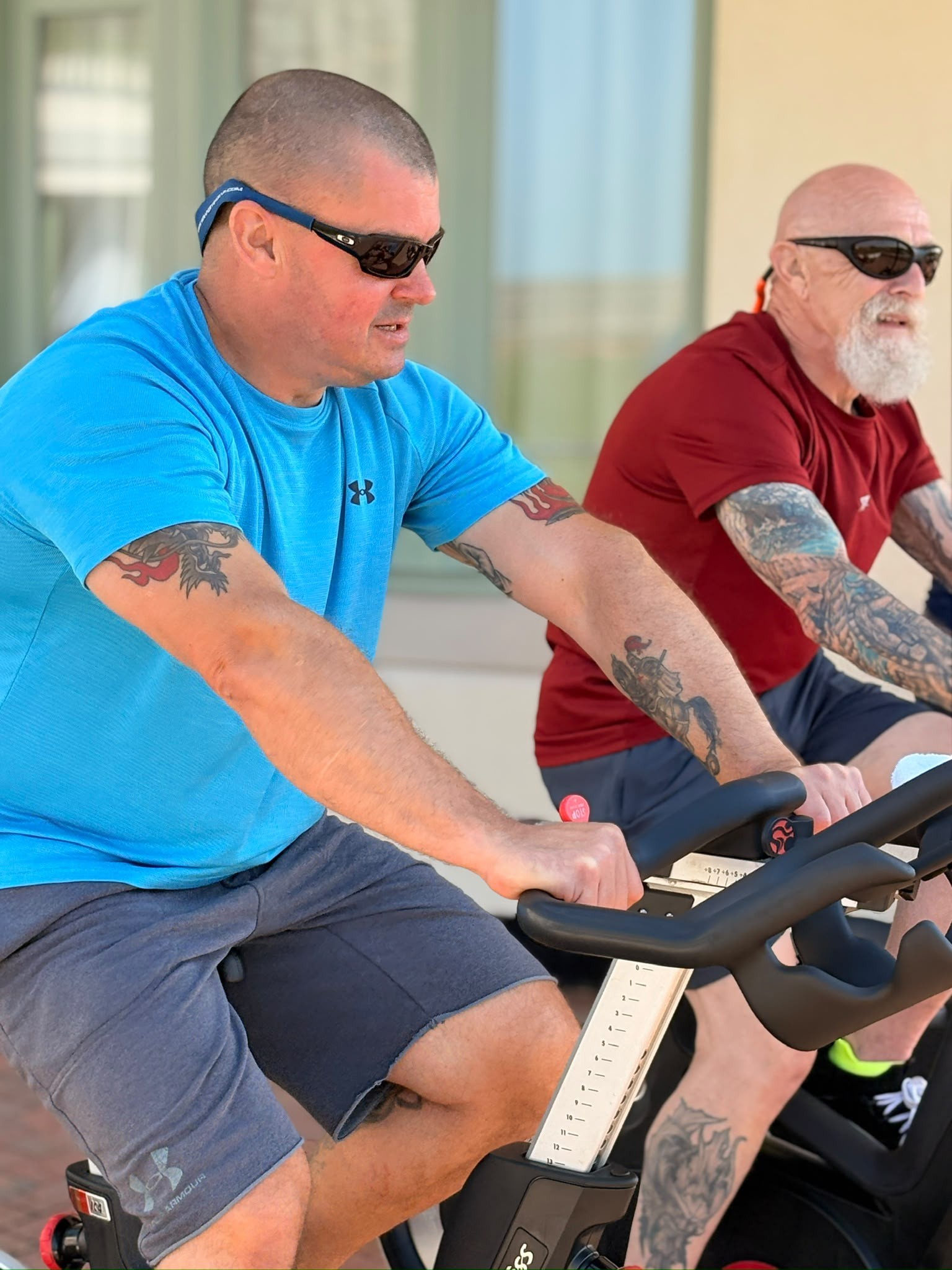 Stu and Jeff on the exercise bikes at the Rustington Centre which have been placed in the garden. Both wearing sunglasses.