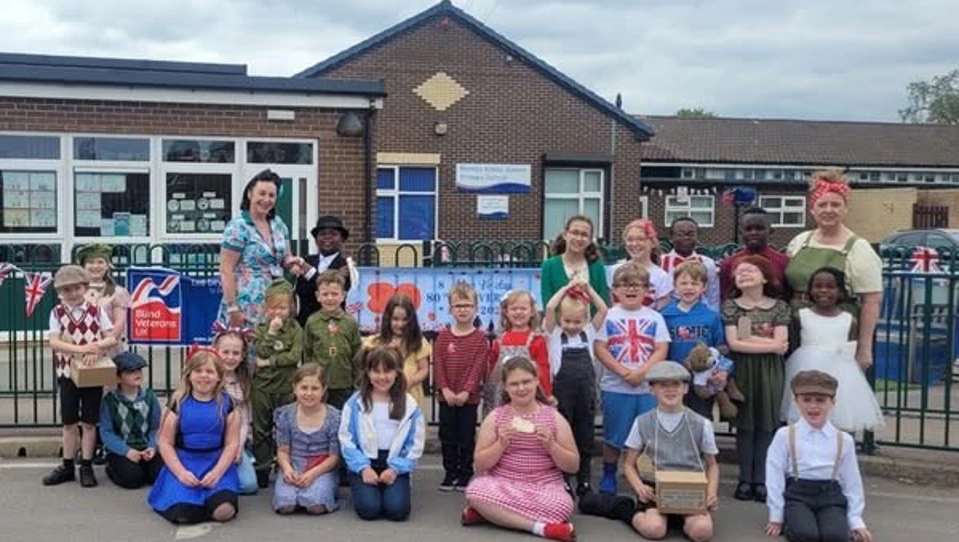 Children and staff pictured with the school in the background wearing party clothes or 1940s inspired outfits