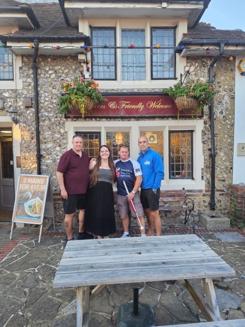 Group of four, including Stu in his Blind Veterans UK t-shirt, are stood outside the front of Ye Olde House at Home to pose for a picture 