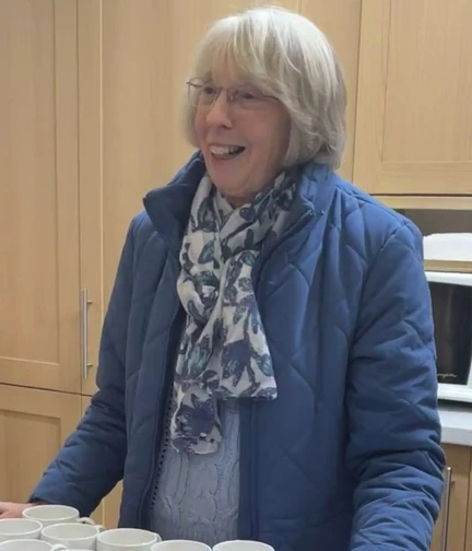 A lady stand behind a counter laid out with tea cups