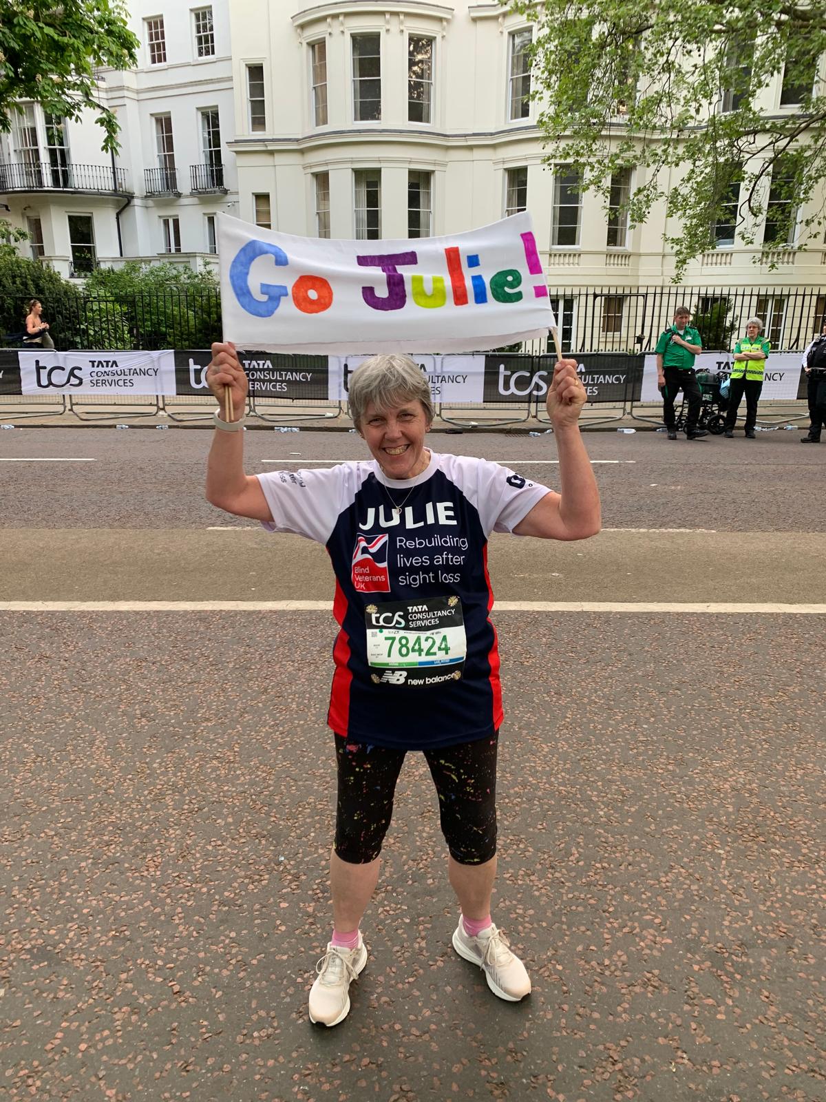 Julie on the streets of London pauses to hold up a sign that reads 'Go Julie'