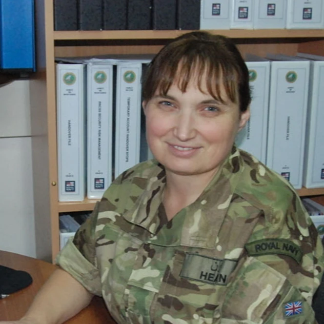 Rosina, dressed in military camouflage with a Royal Navy patch, smiles white seated at a desk.