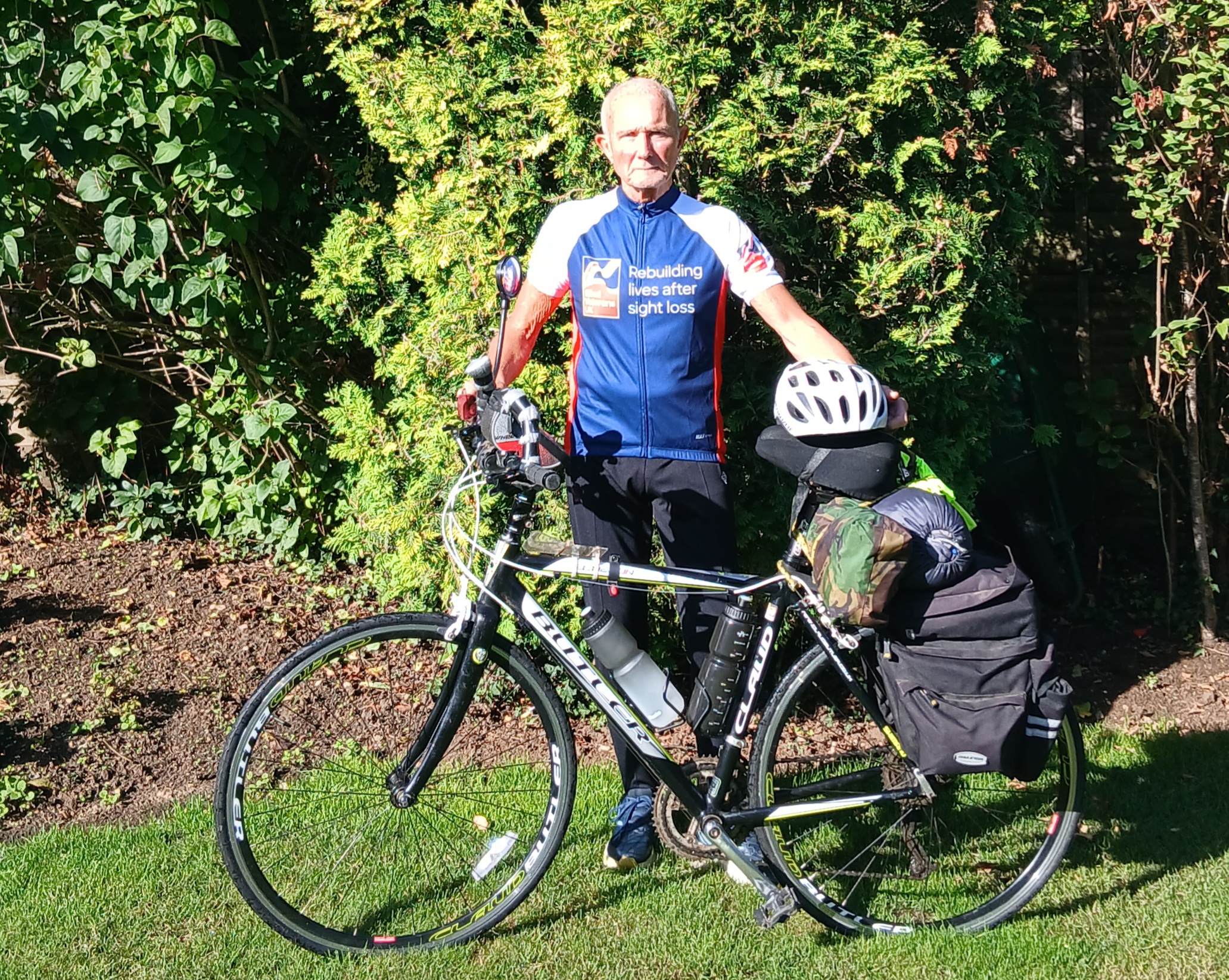 Eddy pictured standing next to his bicycle which is loaded up ready for the challenge. He wears a Blind Veterans UK cycling top