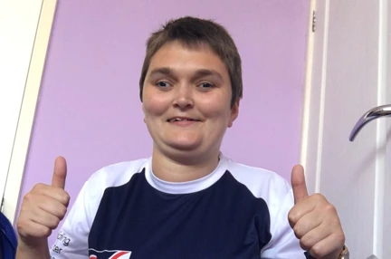 Laura pictured smiling and putting her thumbs up, wearing a Blind Veterans UK top