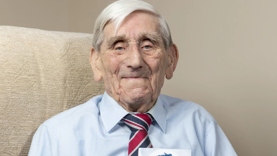 Les sat in a chair holding a framed photo of himself in service