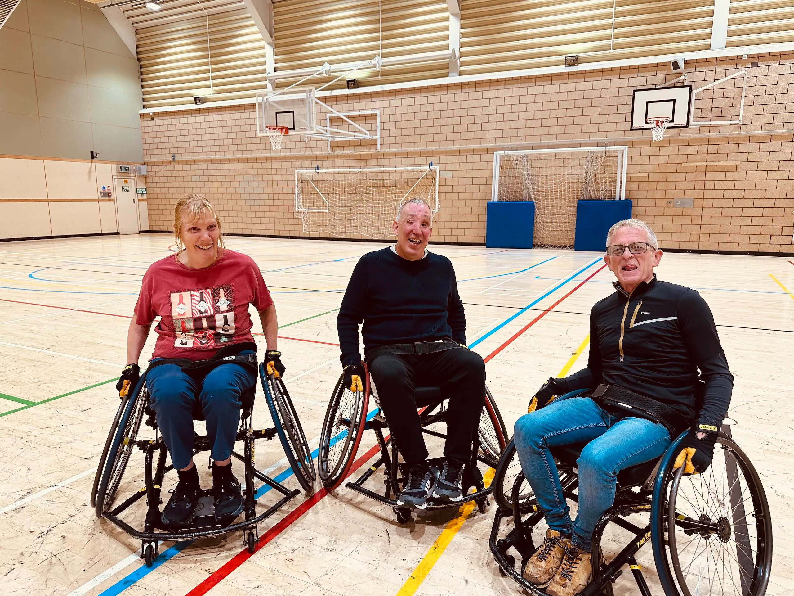 Three blind veterans sit in their wheelchaits on a basketball court and look into the camera, smiling.