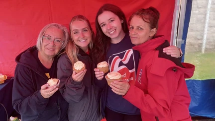 Four women holding up cup cakes and smiling as they gather round for a photo