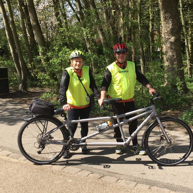 Richard and Maria dressed in high vis tops stood holding up their tandem bike