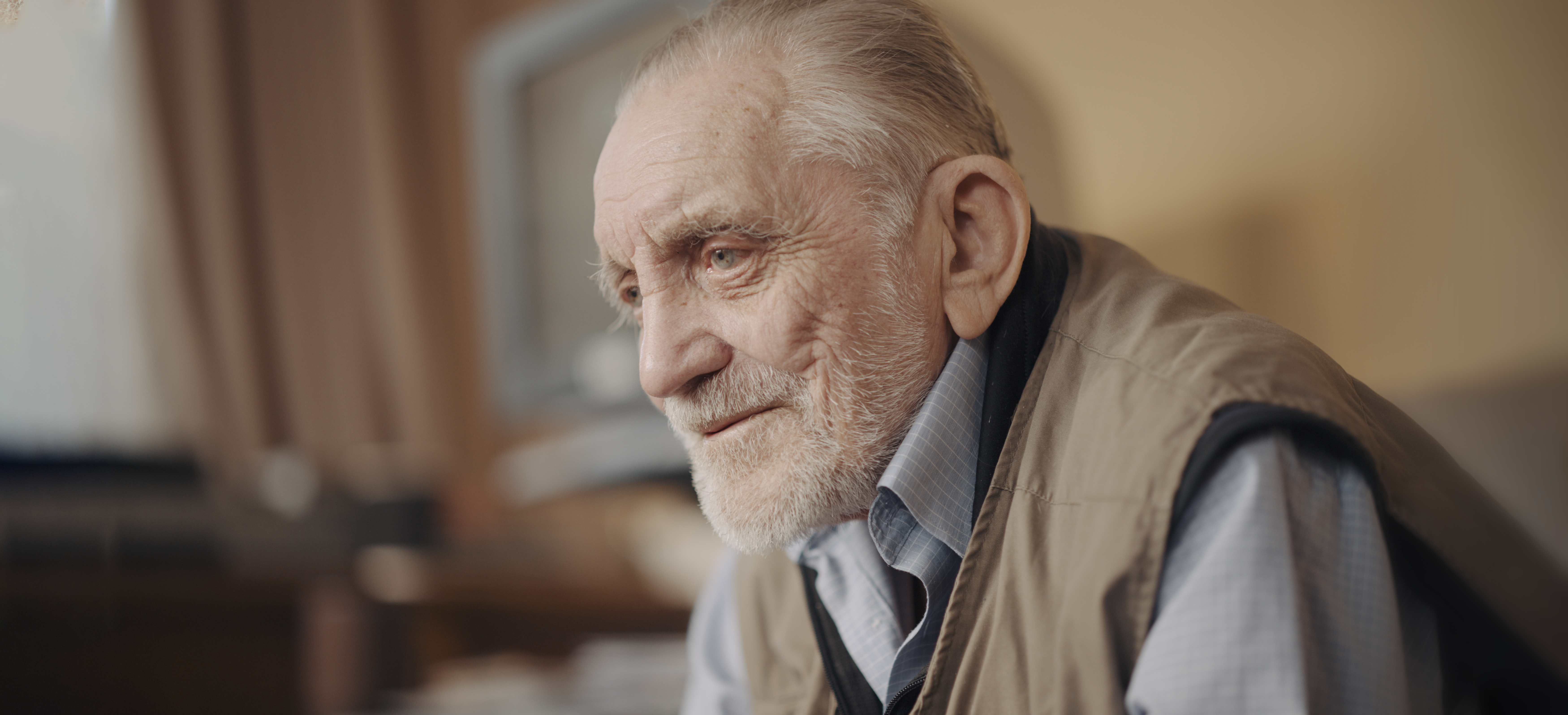 Blind veteran Ken, sitting down in his living room, showing a small smile as he looks across the room