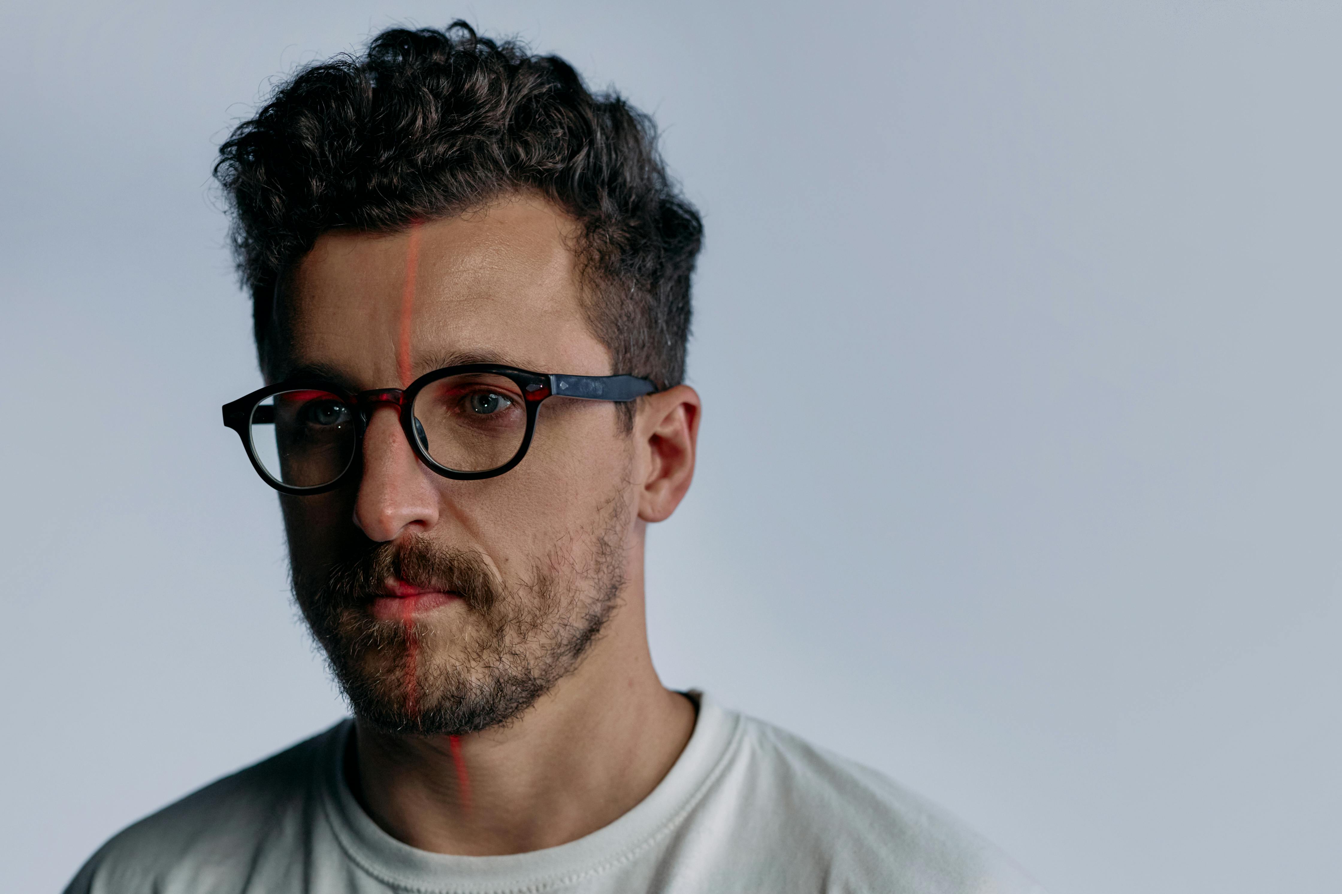 Close-up portrait of a person wearing smart glasses, with a vertical red line visible across one eye against a plain background.
