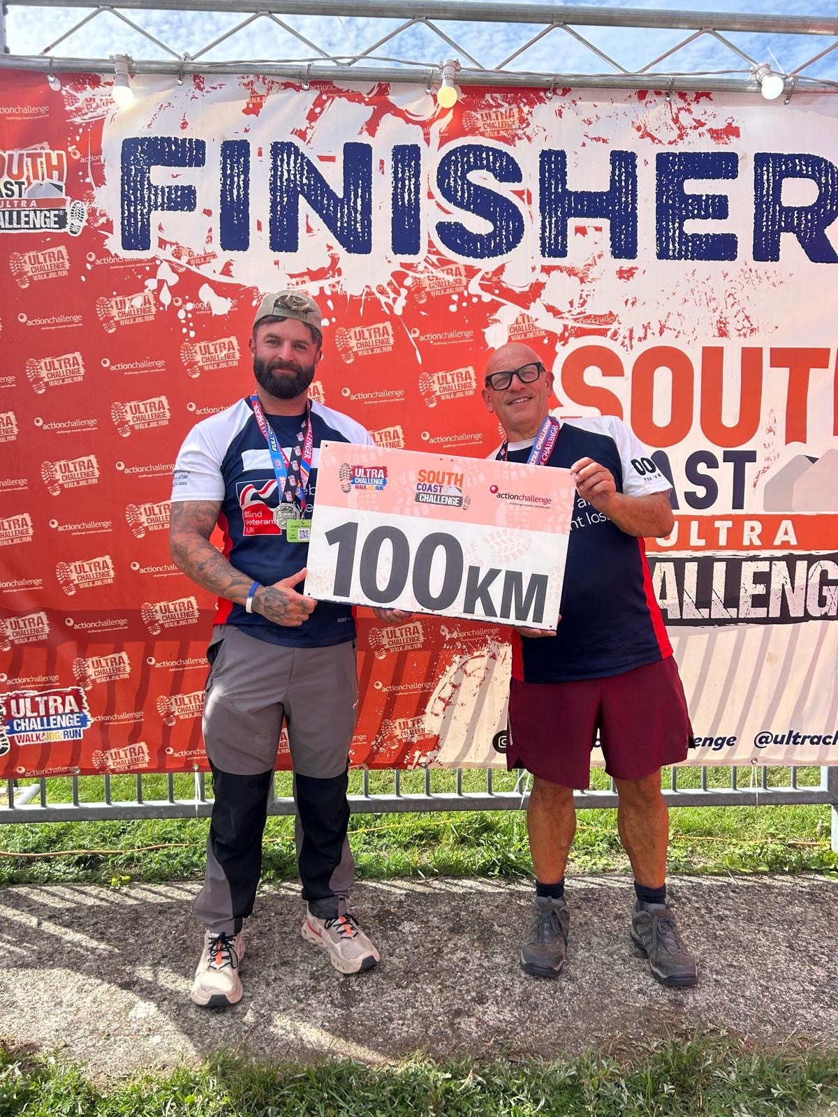 Jerry and Jack standing at the finish banner holding a 100km sign