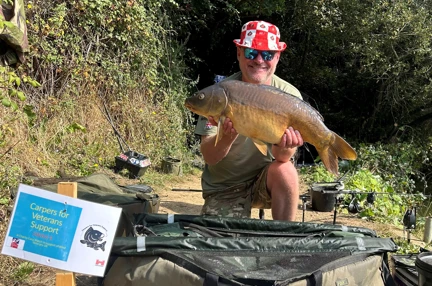 Fisherman kneeling on the ground holding a large fish that he has caught with a sign saying that it weighs 17lb and 4oz