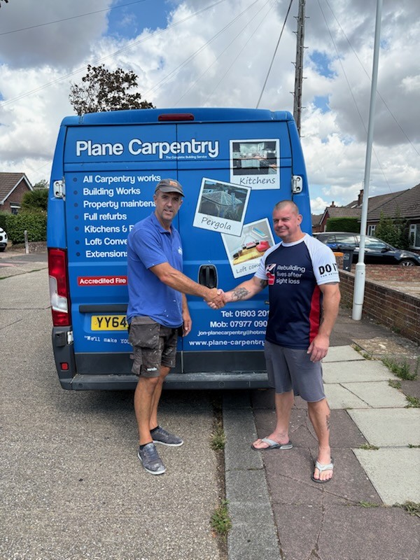 Jon and Stu stood behind Jon's work vehicle shaking hands