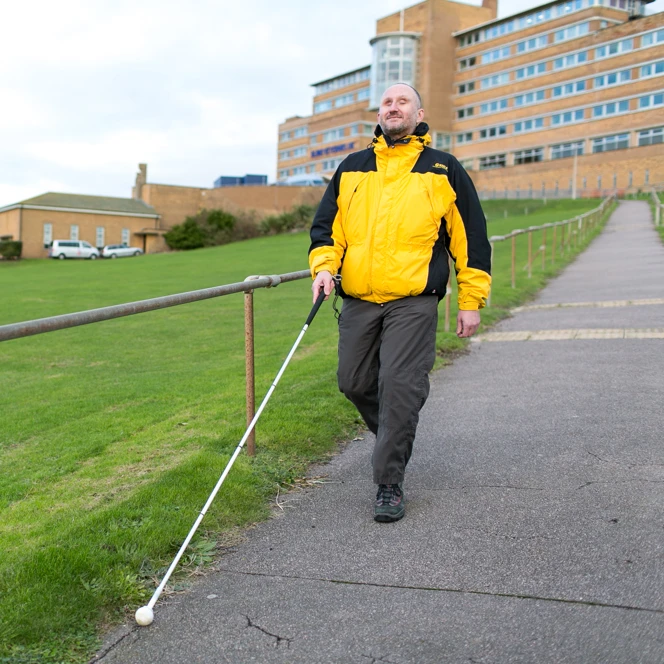 Blind veteran Mark using a guide cane to walk down a path in front of Blind Veterans UK centre of wellbeing