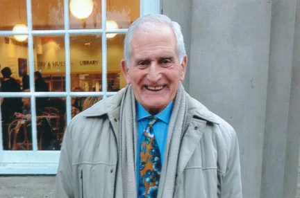 Blind veteran Geoffrey pictured standing outside, wearing a warm coat and smiling to the camera