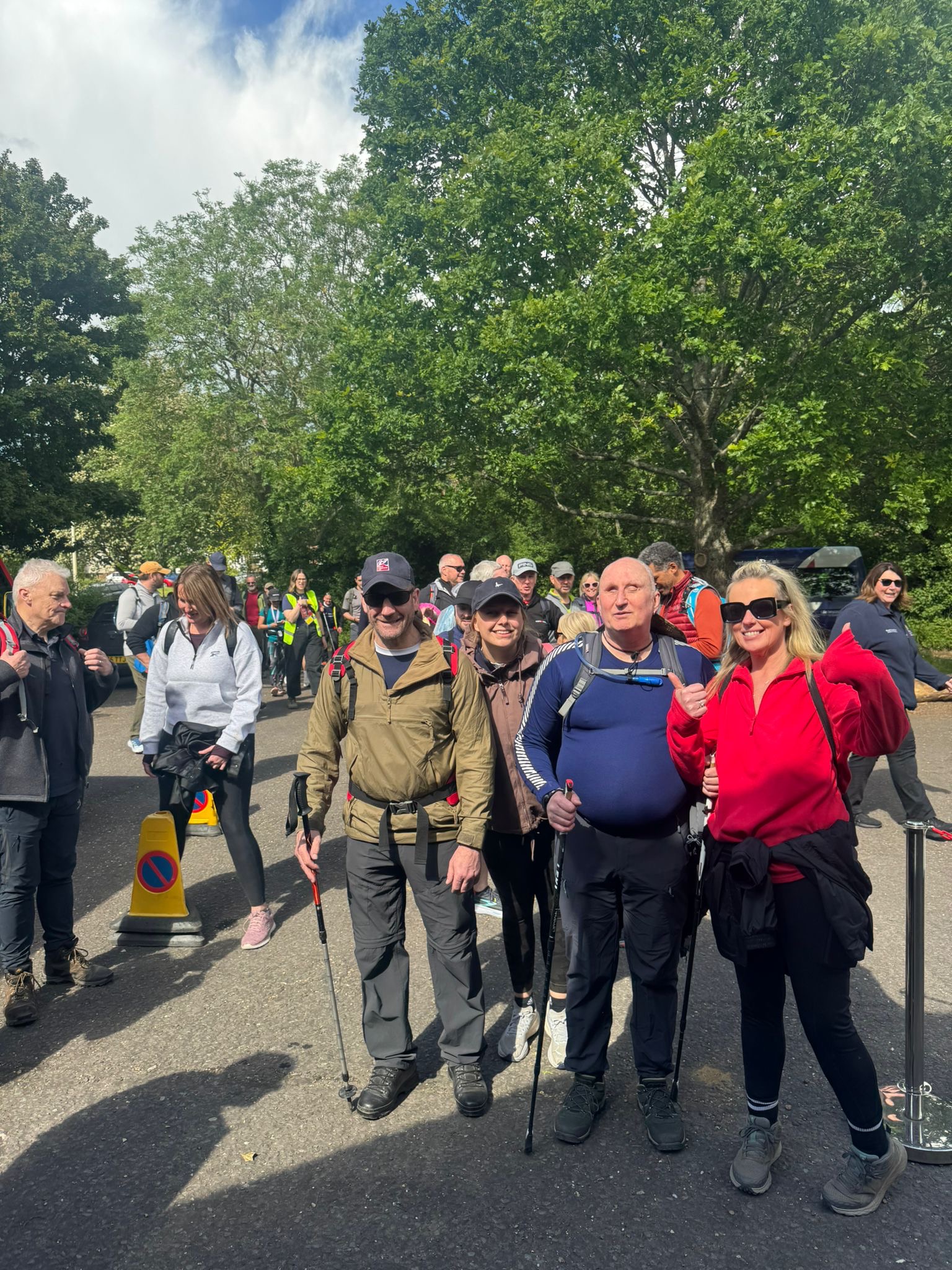 Four Operation Enigma participants standing together outdoors with walking poles, with other walkers gathered behind them.
