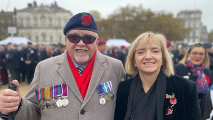 Blind veteran Ron holding a white and wearing medals standing with staff member Glynis