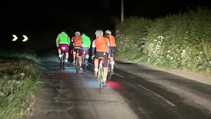 Image from behind the cyclists, who are all wearing high vis tops, as they ride along a road in the dark