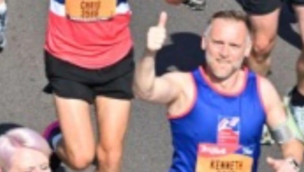 Kenny looks up for the camera while running and gives a smile and a thumbs up.
