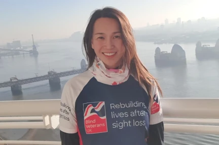 Supporter Roxana stood in front of a misty River Thames wearing her Blind Veterans UK T-shirt