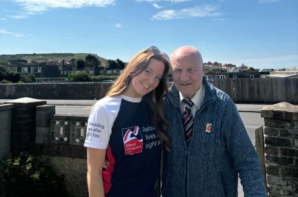 Grace and her grandad stood together. Grace is wearing a Blind Veterans UK t-shirt and Peter is wearing a Blind Veterans UK pin badge
