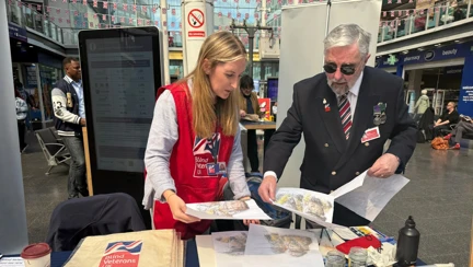 A blind veteran stands at a table covered with VE Day paintings he has created.