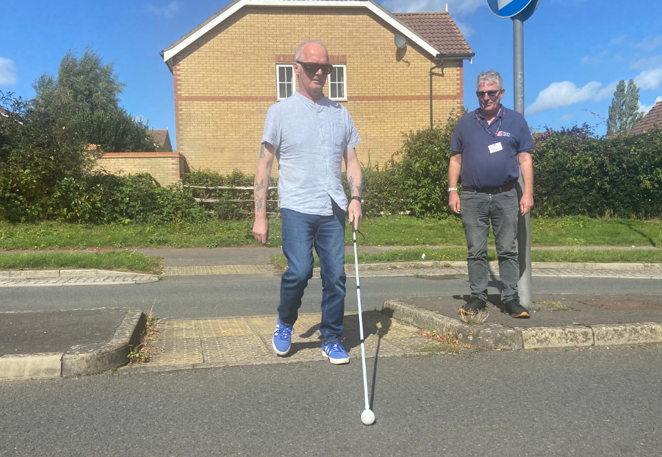 Blind veteran Mark using his long cane to cross the road, assisted by his CSW