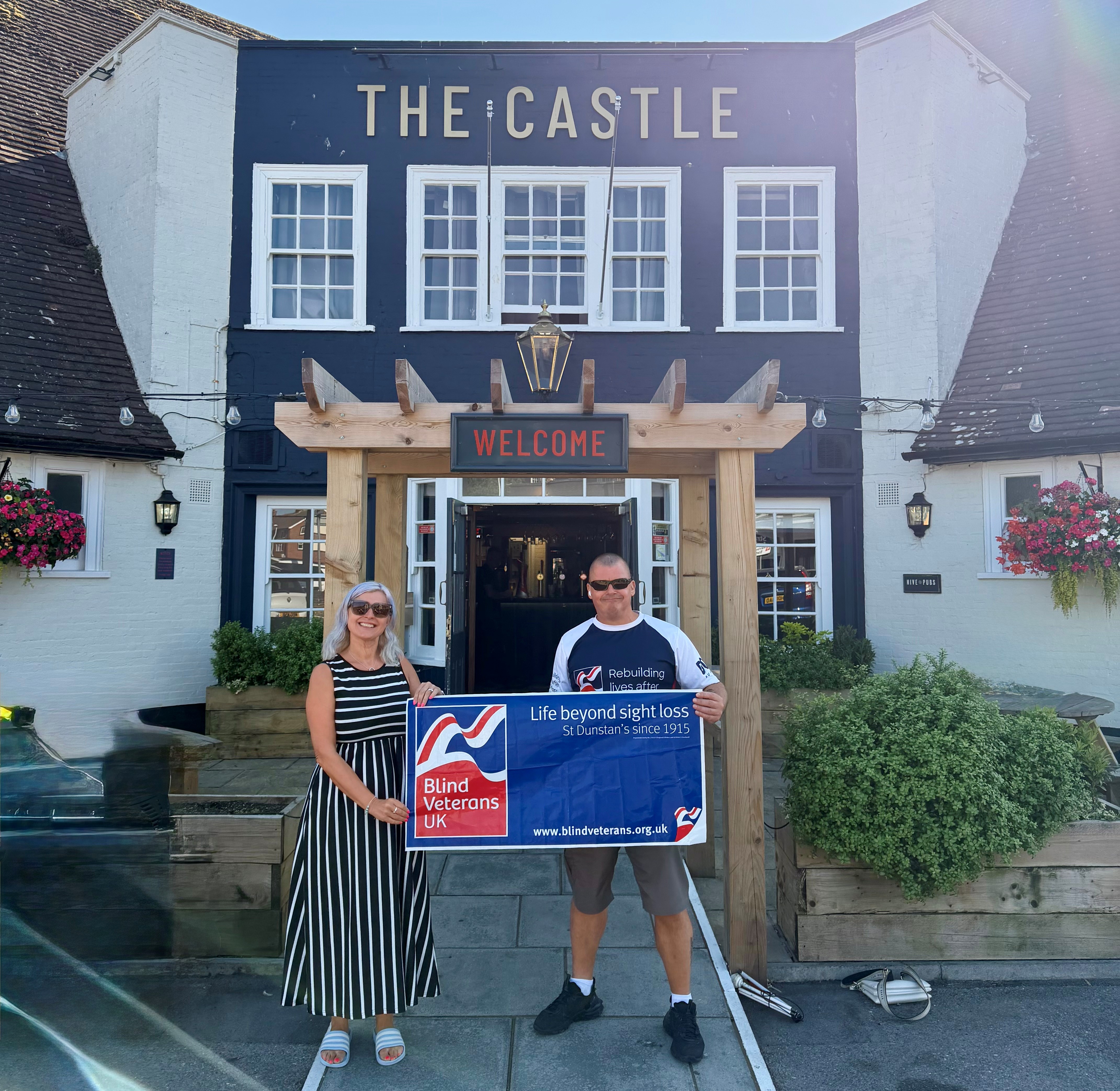 Stu and Mel outside The Castle pub with a Blind Veterans UK banner