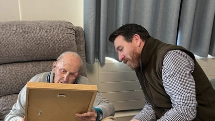 Ken is holding the framed illustration and Tim is leaning in describing it to Ken