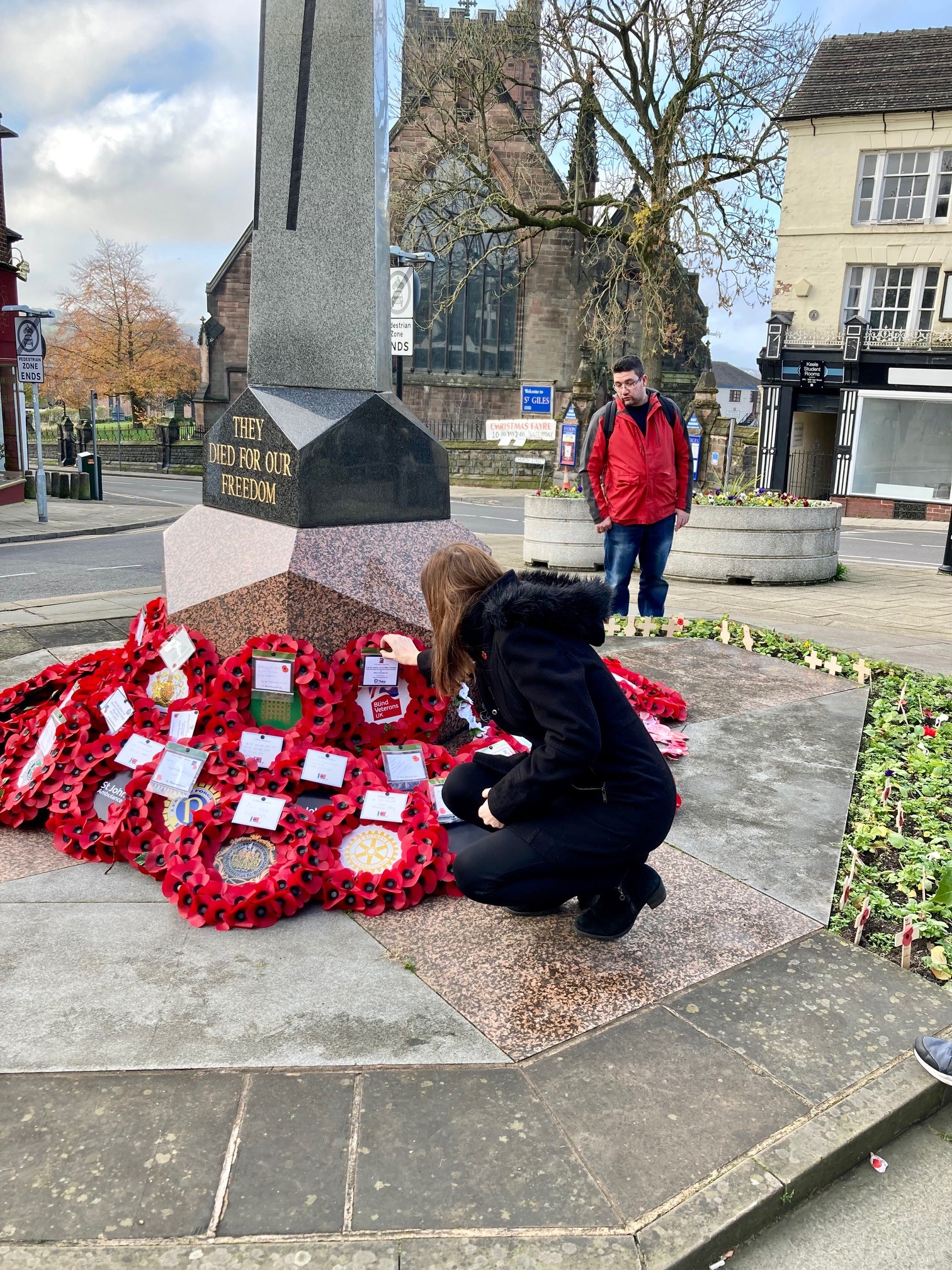 Stephanie knelt down placing a poppy wreath alongside others at a war memorial