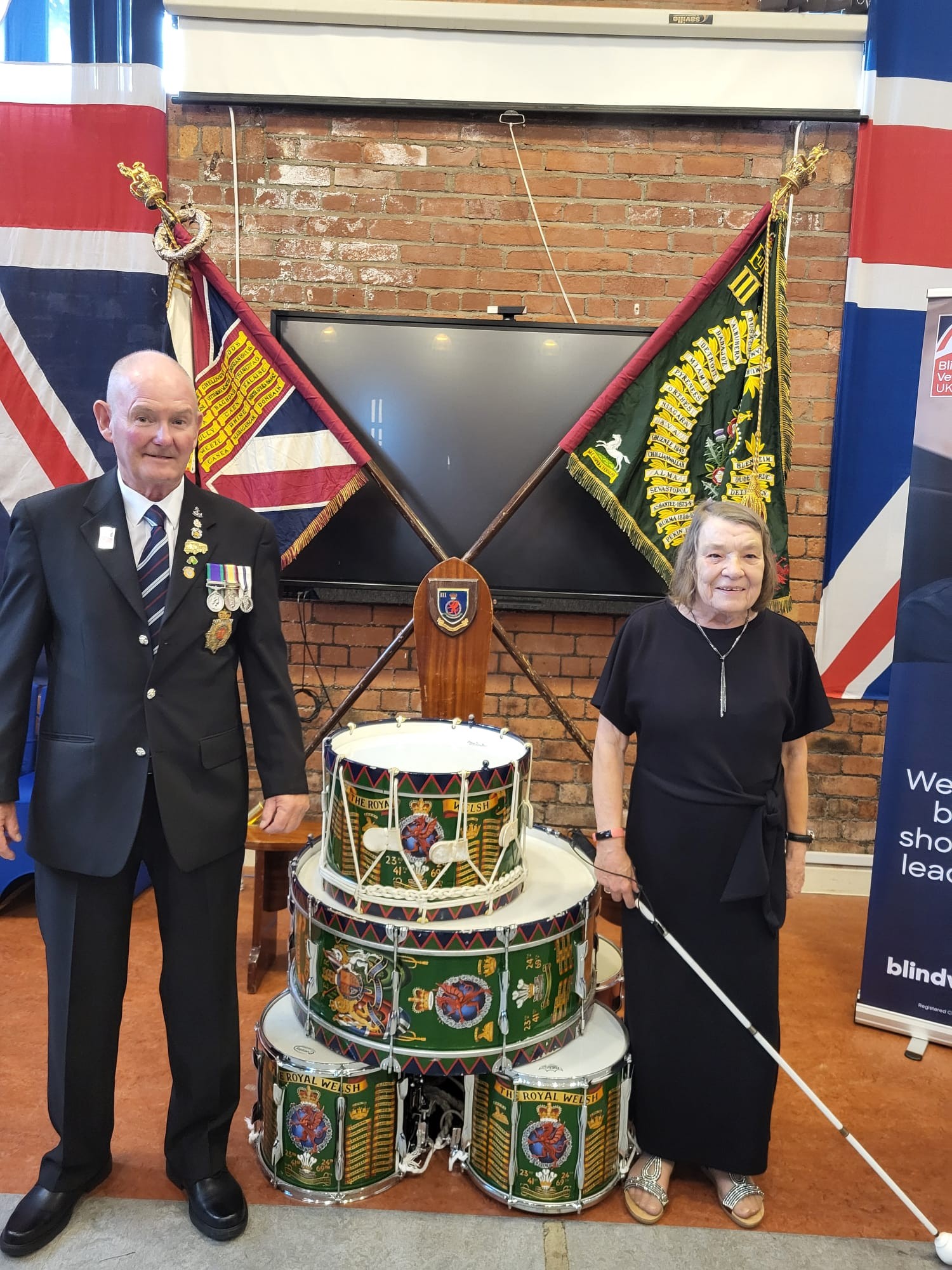 Noeline and John in their best clothes stood either side of military drums