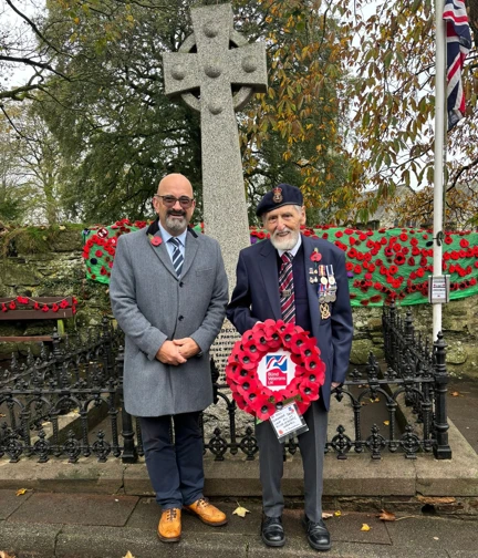Blind veteran John standing in front of a memorial preparing to lay a wreath with staff member Peter