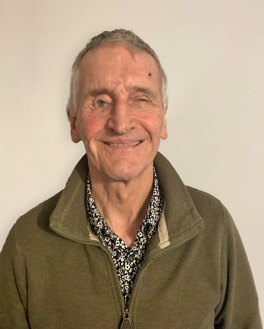 Colour portrait photo of blind veteran Jamie against a neutral backdrop, smiling at the camera