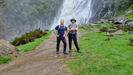 Steve and Chris are stood together in their walking gear in front of a waterfall