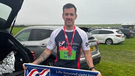 Garry in his Blind Veterans UK running top and holding a Blind Veterans UK banner