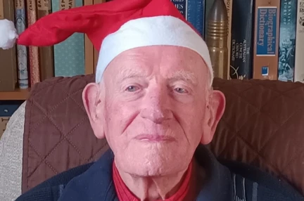 Mike smiling, wearing a Santa hat and holding some colourful tinsel.