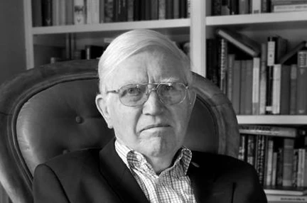 A black and white photo of Dr Zbigniew Pelczynski OBE sitting in chair with bookshelf in background