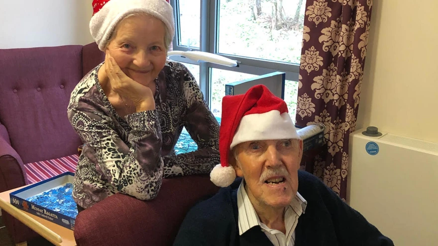 Blind veteran Bill and his wife, smiling and wearing Christmas hats
