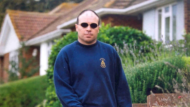 Blind veteran Billy wearing dark sunglasses and using a long white cane as he walks along a path