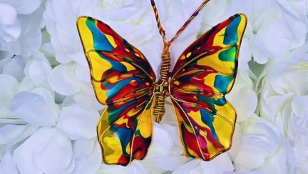 A vibrant resin butterfly with yellow, red and blue waves of colour against a white flowerbed