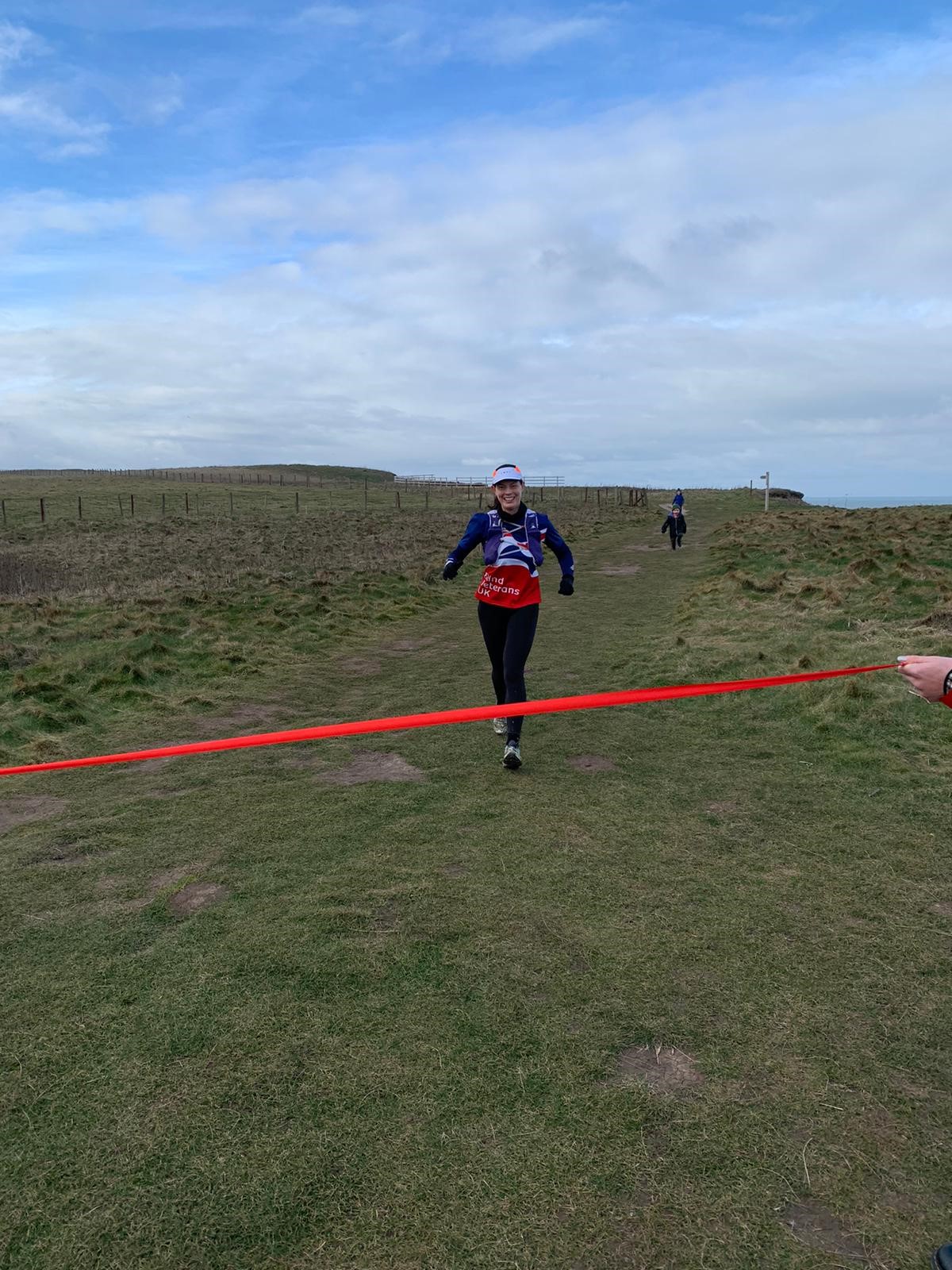 Rachel smiling as she runs towards a red finish line being held by her family