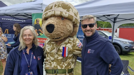 A person wearing a bear costume dressed in military camouflage joined by two members of Blind Veterans UK staff