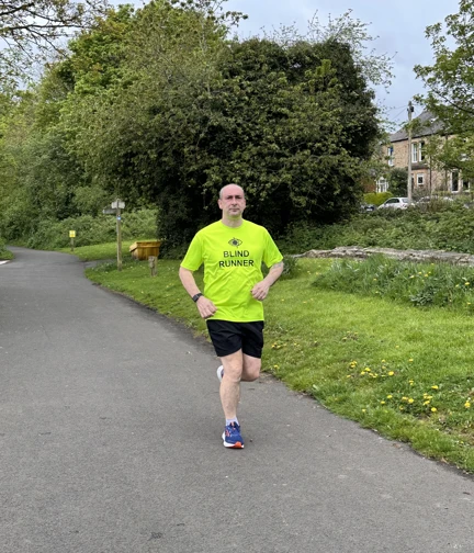 Steve is running along a country lane wearing a bright yellow t-shirt which says "Blind Runner"