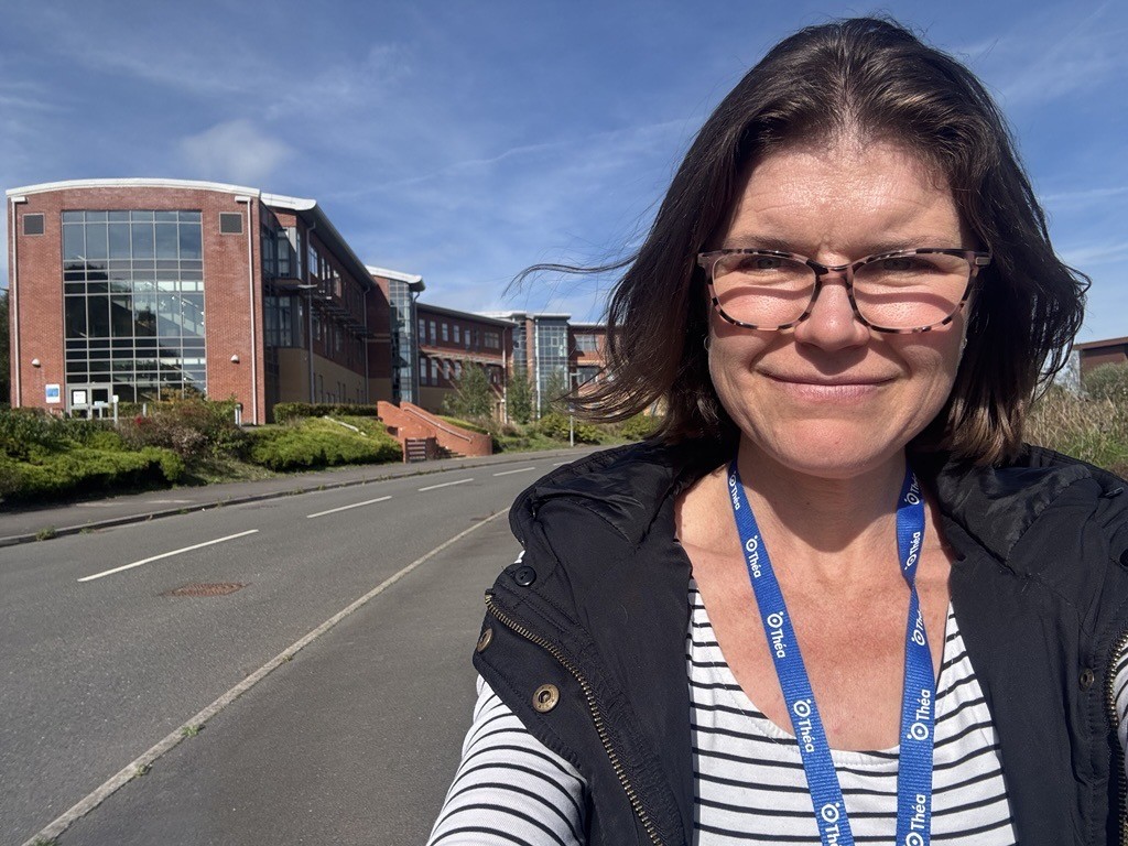 Kate takes a selfie while out for a walk during her lunchbreak. She is walking past office buildings while wearing her Thea lanyard