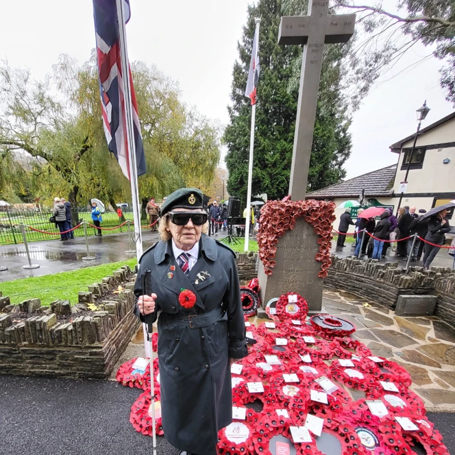 Noeline stood with her white cane in front of the War Memorial with a sea of poppy wreaths at its base