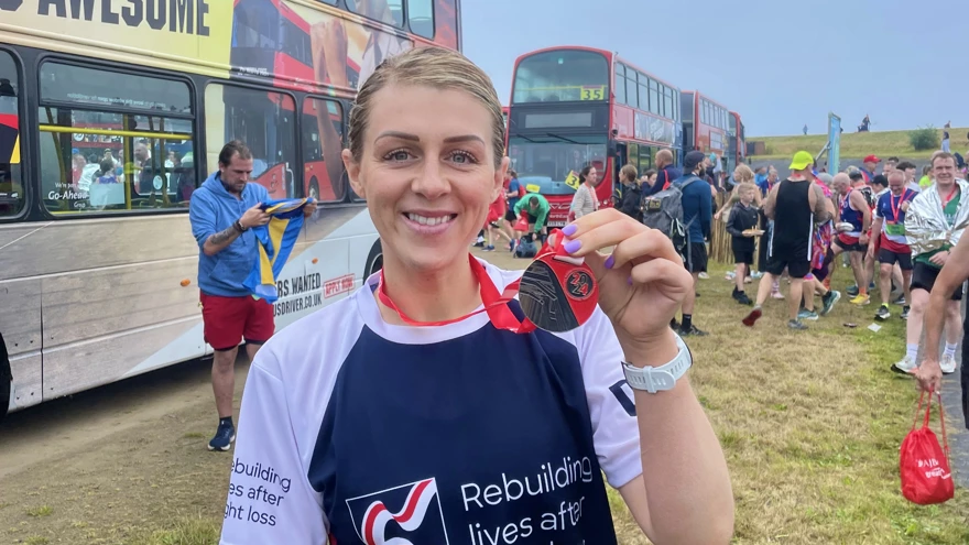 Rachel in her Blind Veterans UK running top has her medal around her neck and is holding it up with one hand to show it to the camera.