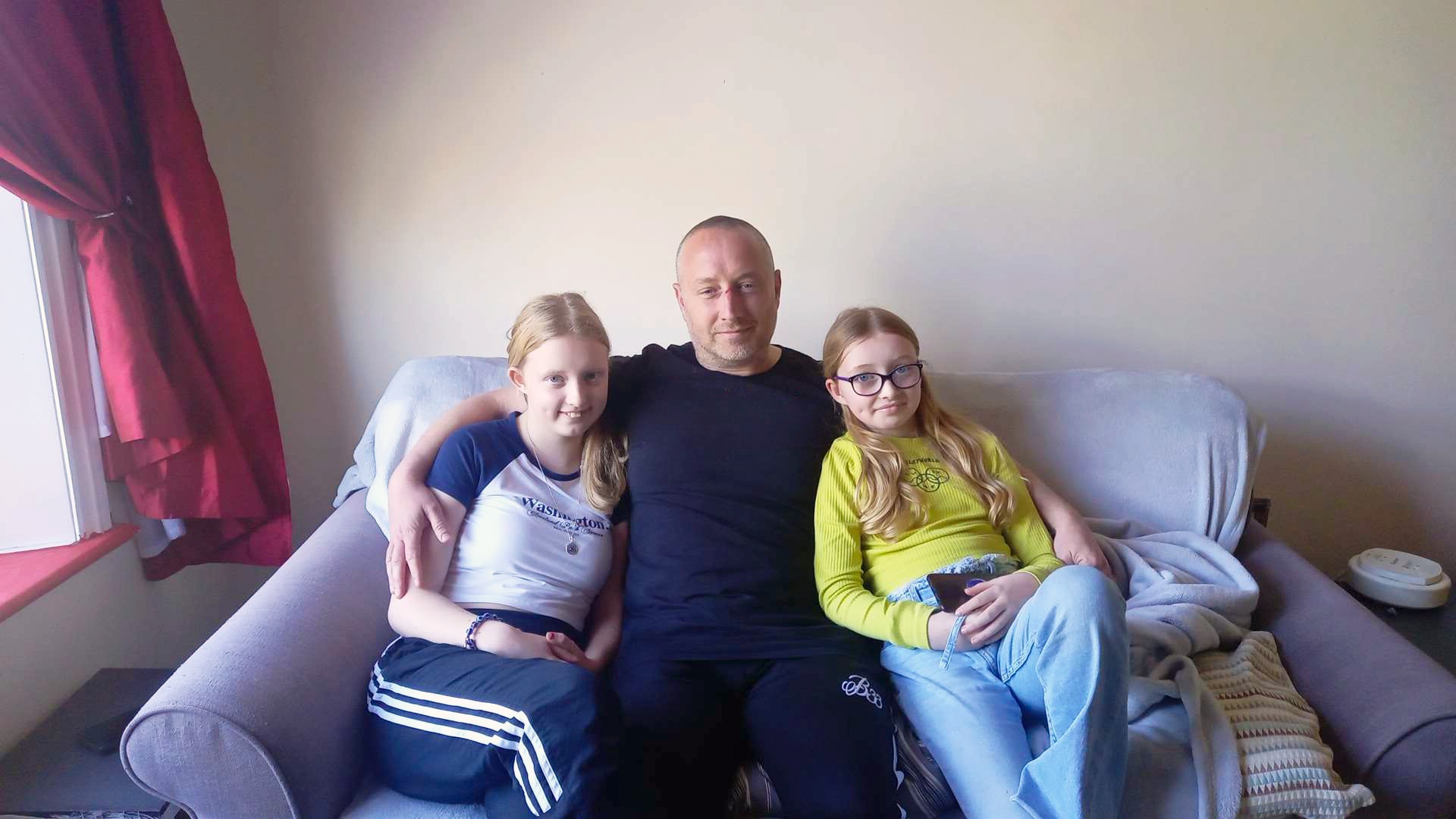 Ian sat cuddling together with his two daughters on the sofa