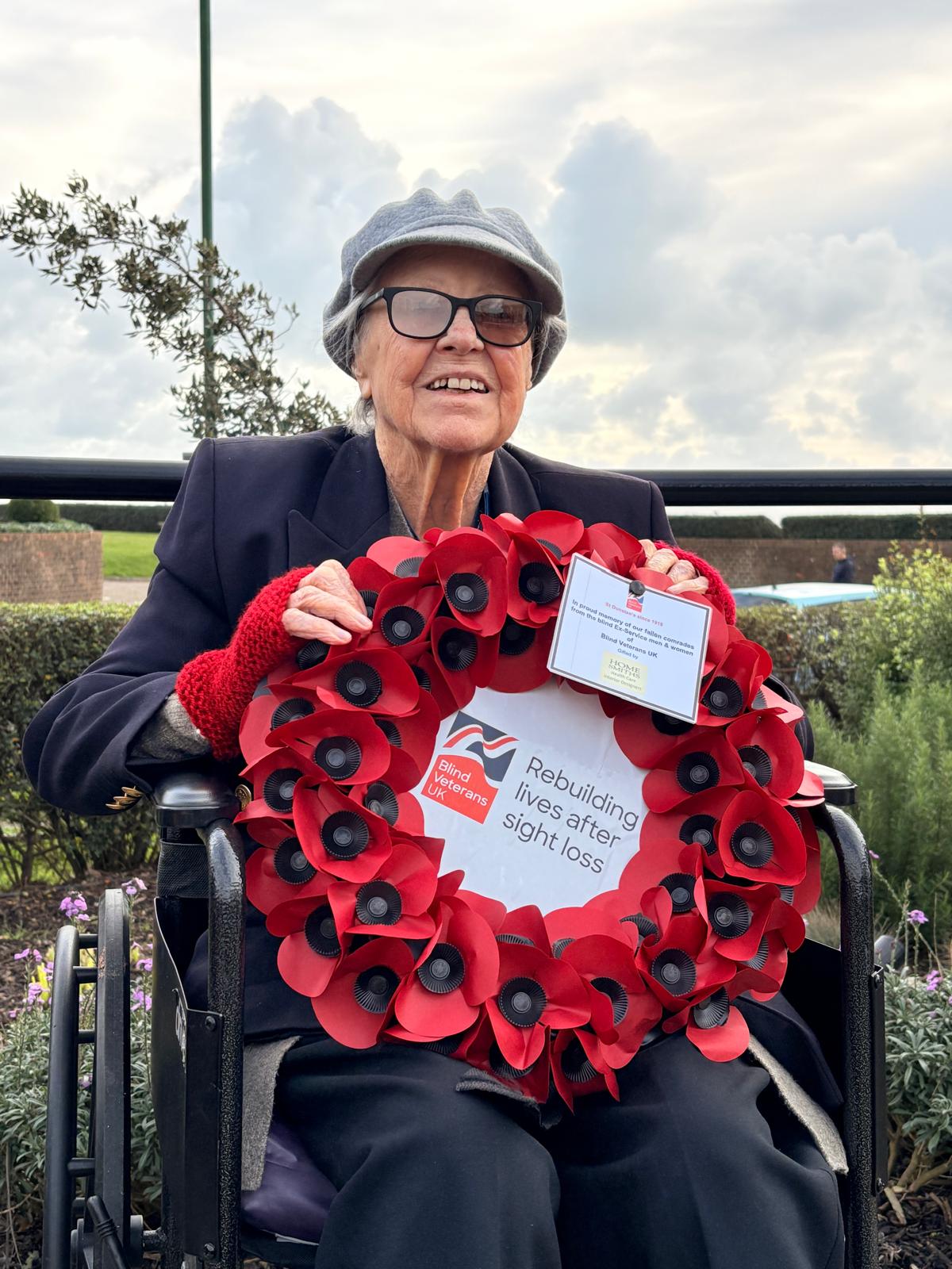 Nancy sits in a wheelchair and looks into the camera, holding a wreath with both hands