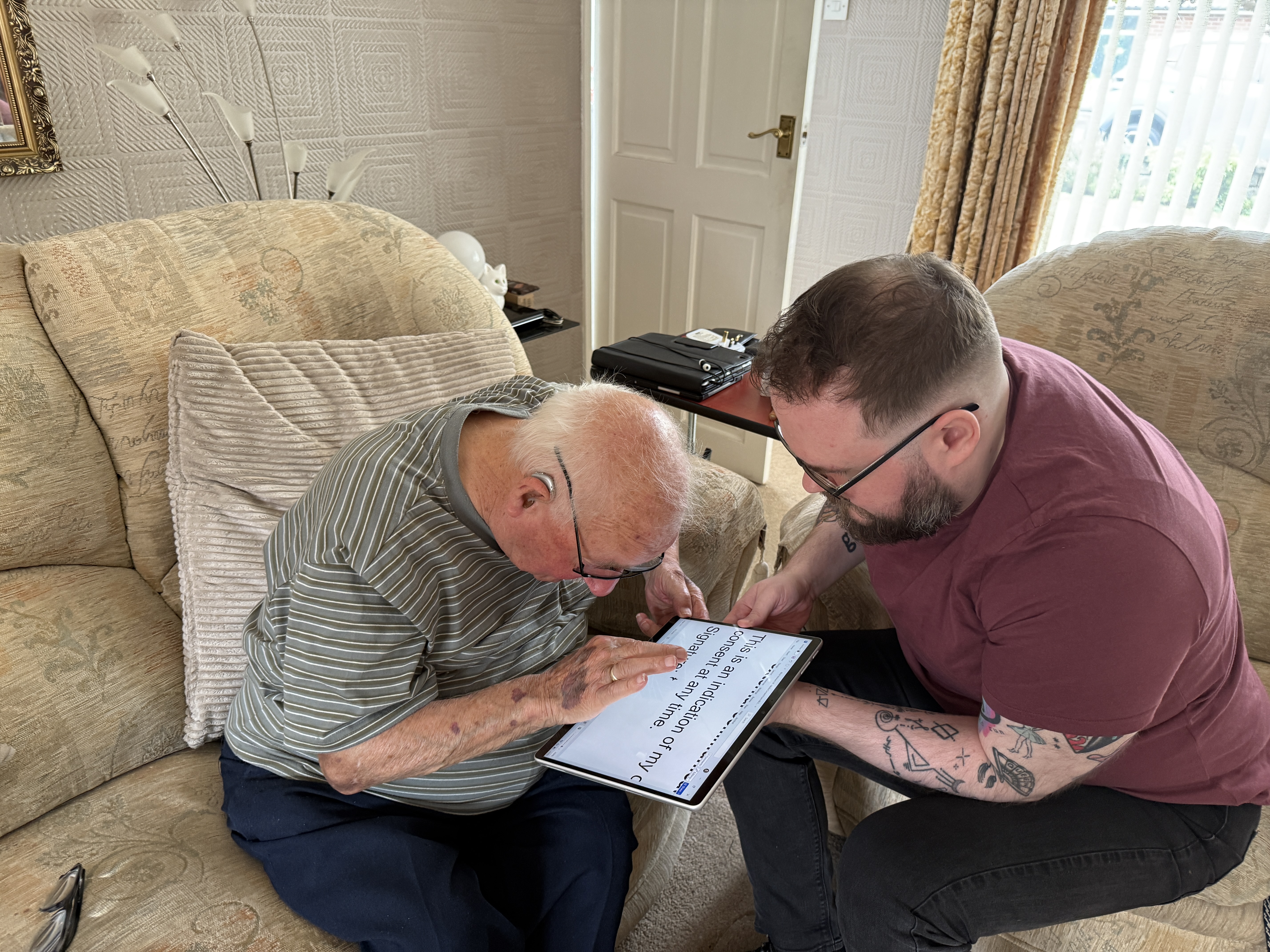 Ken and David sit close together, reading information on a tablet during a home visit.