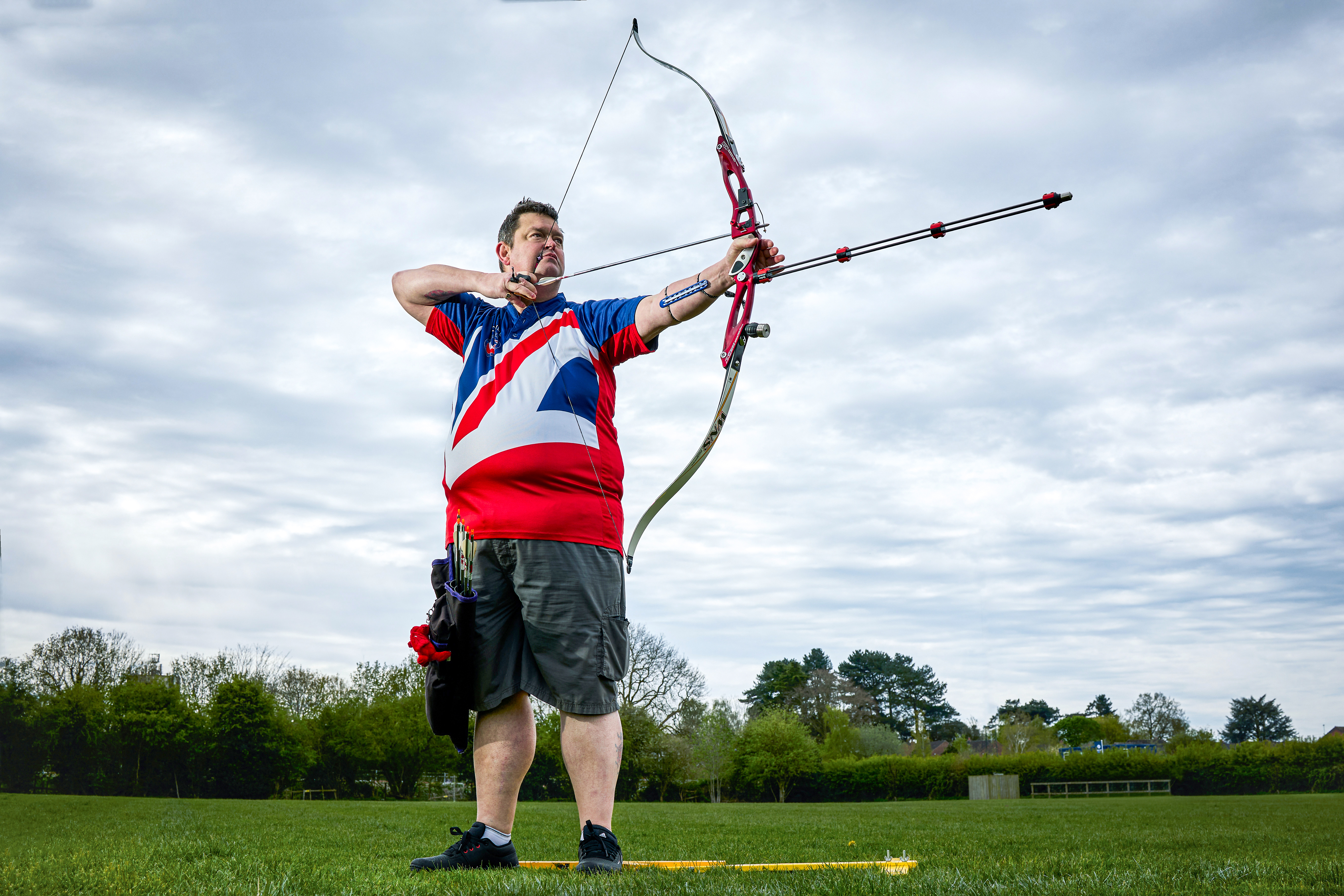 An image of Clive in his GB Archery T-shirt. He stands on the archery field at full draw ready to take his shot